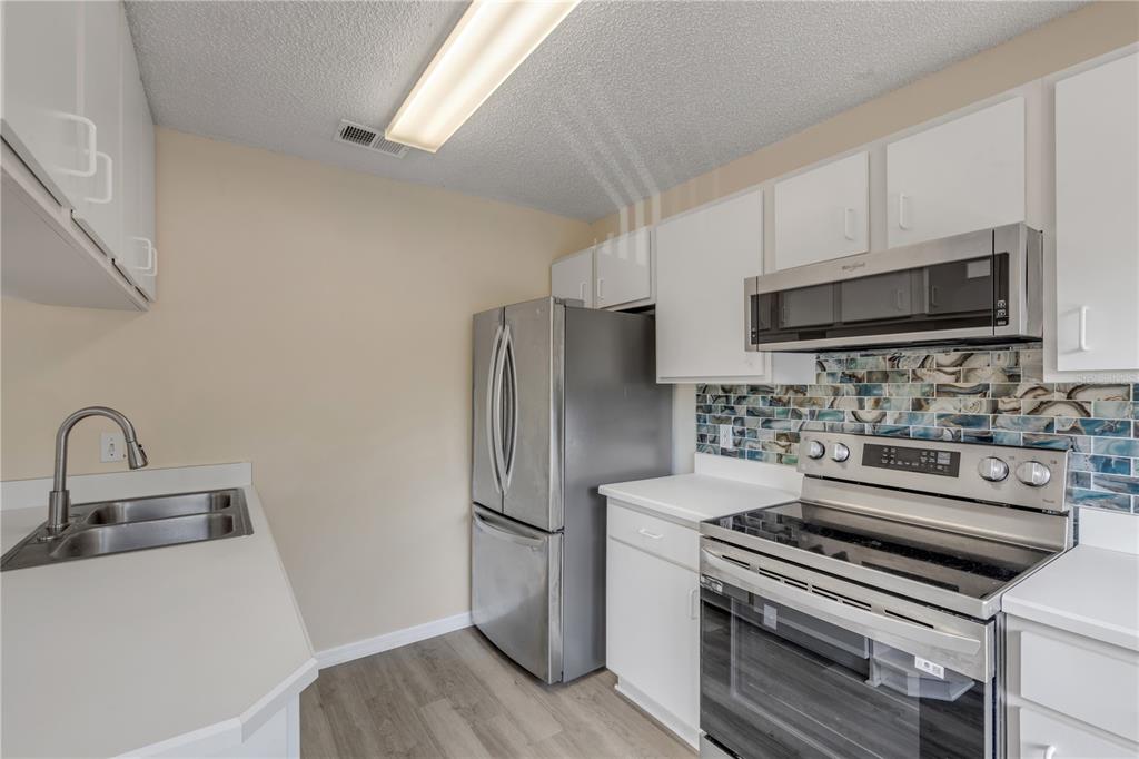 A kitchen featuring white cabinets, stainless steel appliances, and a blue patterned tile backsplash — 1601 BIG TREE ROAD UNIT 807, SOUTH DAYTONA, FL