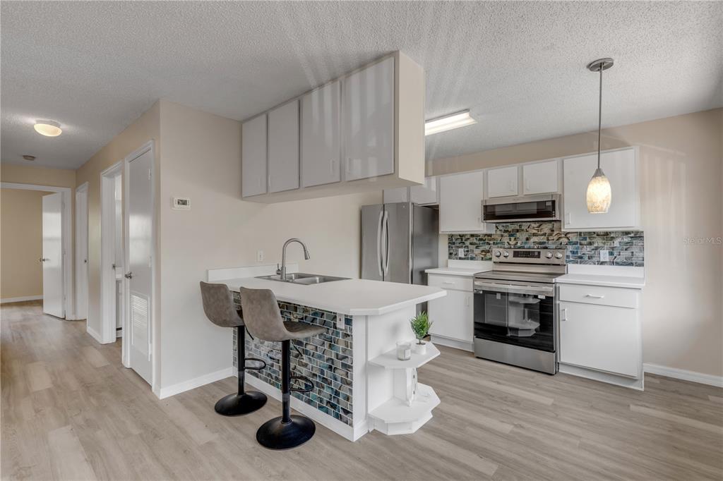A kitchen features white cabinets, stainless steel appliances, a tiled island, and light wood flooring — 1601 BIG TREE ROAD UNIT 807, SOUTH DAYTONA, FL