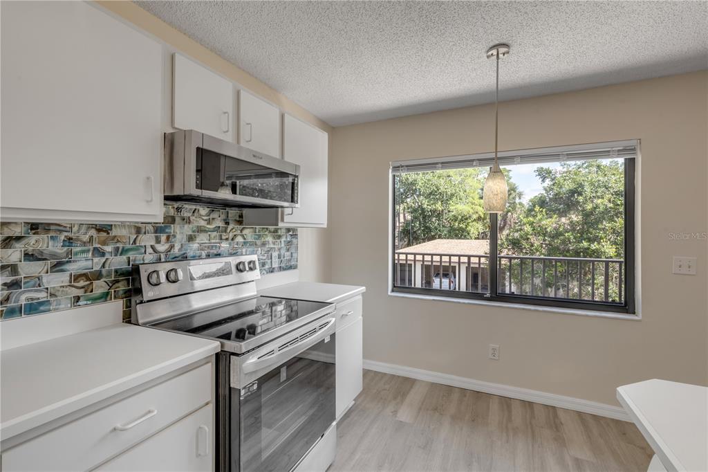 A kitchen features white cabinets, a glass tile backsplash, stainless steel appliances, and a window — 1601 BIG TREE ROAD UNIT 807, SOUTH DAYTONA, FL