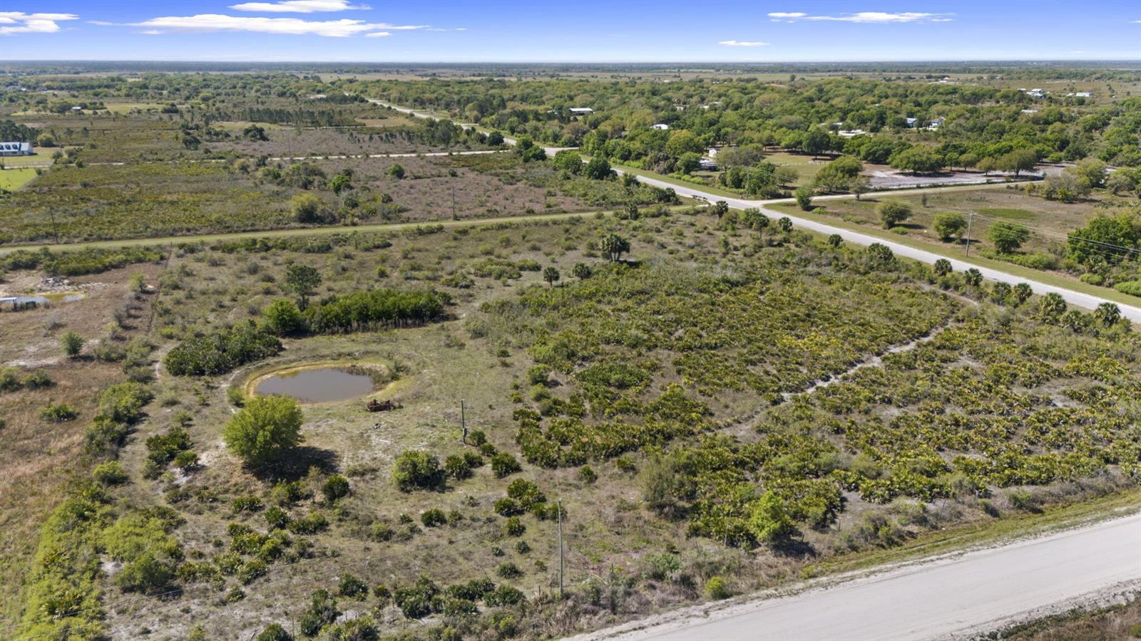 An aerial view shows a large, grassy, undeveloped lot featuring a small pond and trees — 19050 NW 256th Street, Okeechobee FL 34972, OKEECHOBEE, FL