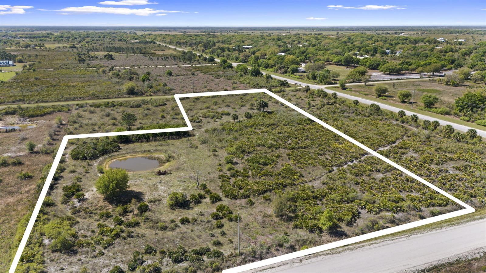An aerial view shows a vacant, brush-covered lot with a small pond and road access — 19050 NW 256th Street, Okeechobee FL 34972, OKEECHOBEE, FL