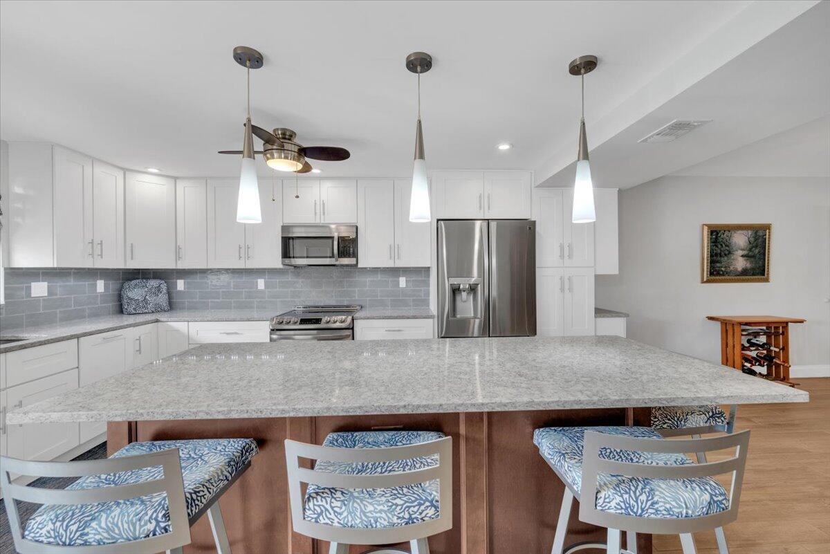 A kitchen features white cabinets, a large granite island, and blue patterned bar stools — 300 N Hwy A1a # 101h, Jupiter FL 33477, JUPITER, FL