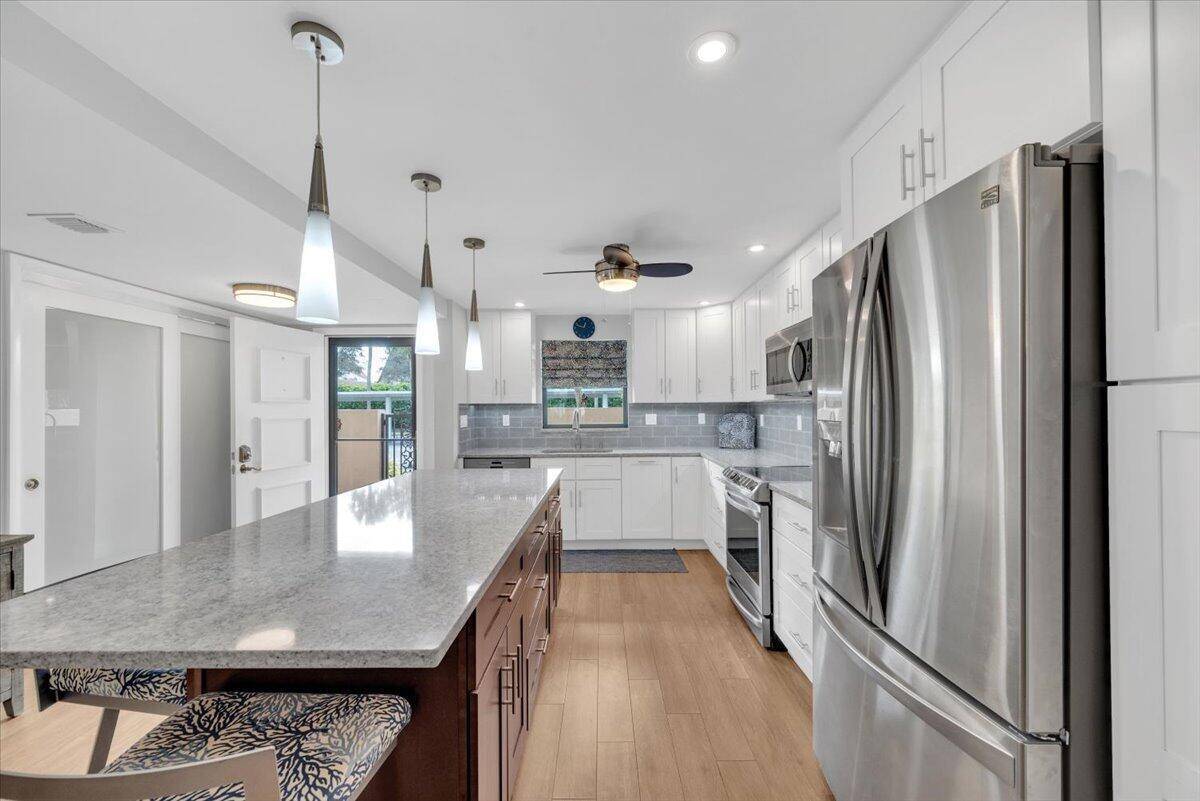 A modern kitchen features white cabinets, a large granite island, and stainless steel appliances — 300 N Hwy A1a # 101h, Jupiter FL 33477, JUPITER, FL