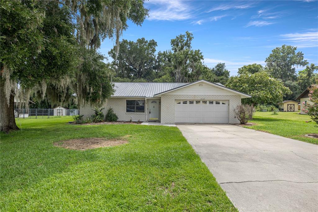 A single-story brick house with a metal roof, attached garage, and a large front lawn — 12185 SE 61ST COURT, BELLEVIEW, FL