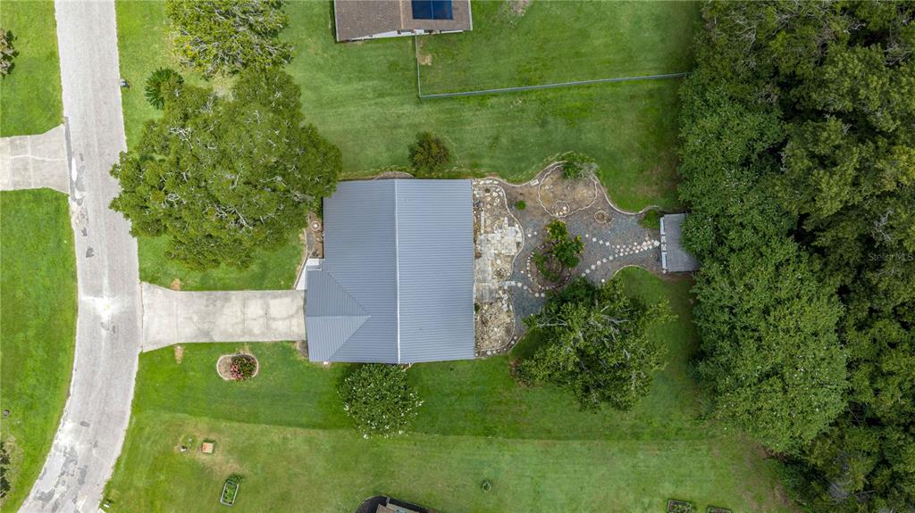 An aerial view shows a house with a metal roof, stone patio, and surrounding lawn — 12185 SE 61ST COURT, BELLEVIEW, FL