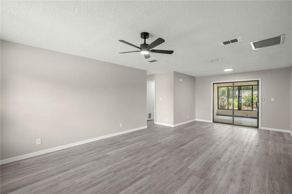 A spacious, empty living room with light gray walls, wood-look flooring, and a ceiling fan — 12185 SE 61ST COURT, BELLEVIEW, FL