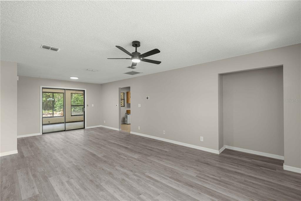 An empty living room features light gray walls, wood-look flooring, a ceiling fan, and sliding doors — 12185 SE 61ST COURT, BELLEVIEW, FL