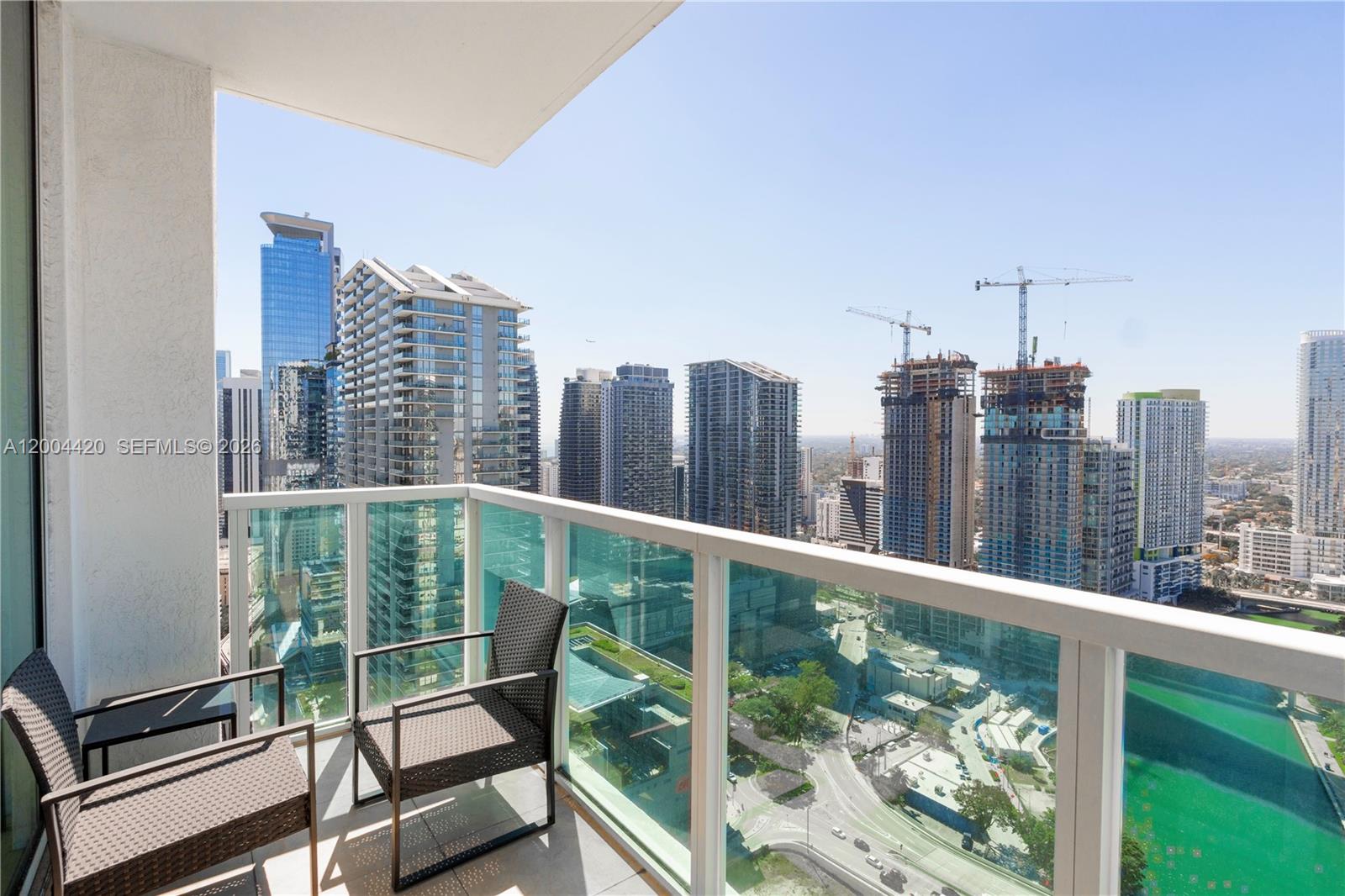 A balcony with two chairs overlooks a dense urban cityscape with several high-rise buildings — 31 SE 5th St # 4121, Miami FL 33131, MIAMI, FL