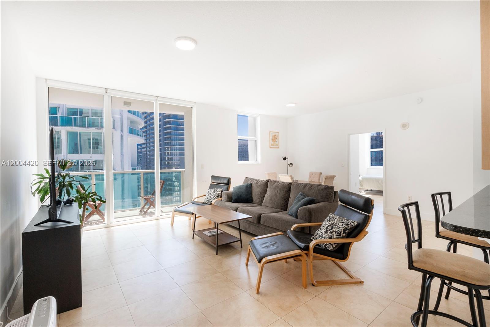 A living room features tile floors, a gray sofa, black armchairs, and a balcony view — 31 SE 5th St # 4121, Miami FL 33131, MIAMI, FL
