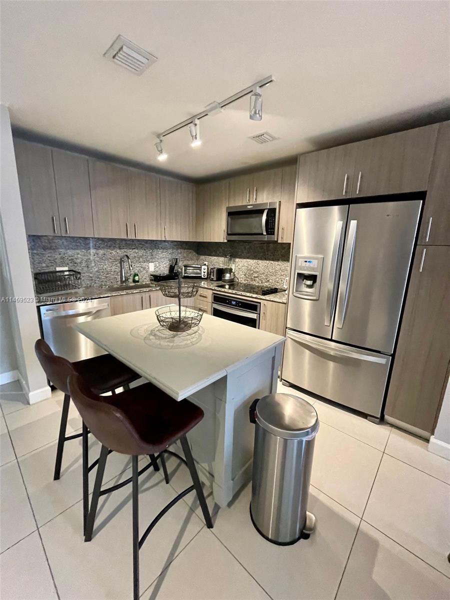 A kitchen features light wood cabinets, stainless steel appliances, a central island, and tile flooring — 5350 NW 84th Ave # 1514, Doral FL 33166, DORAL, FL