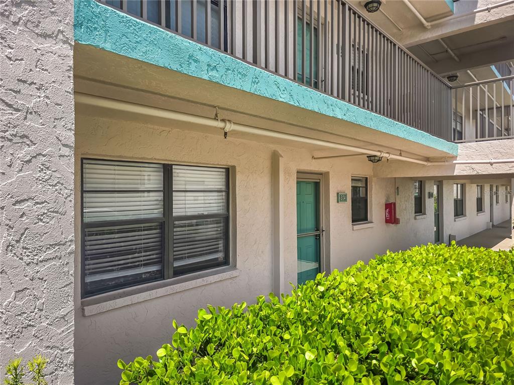 An exterior view of a ground-floor apartment unit with a teal door and window trim — 175 KINGS HIGHWAY Bldg 3 UNIT 314, PUNTA GORDA, FL