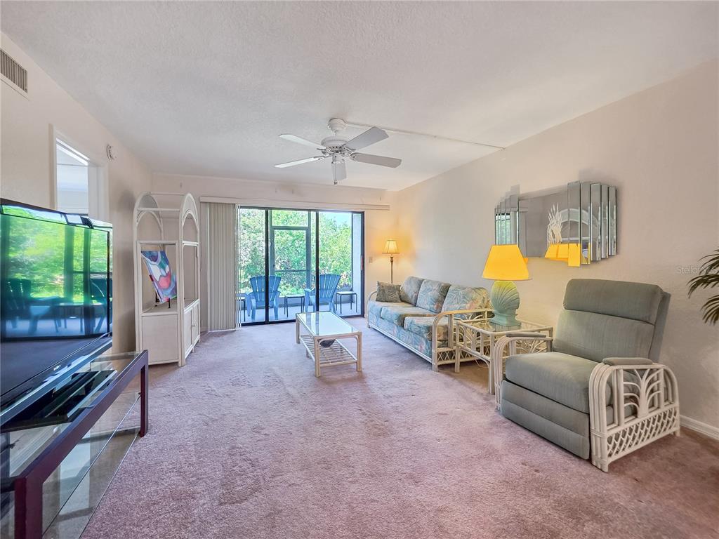 A living room features a pink carpet, floral sofa, light blue recliner, and sliding glass doors — 175 KINGS HIGHWAY Bldg 3 UNIT 314, PUNTA GORDA, FL