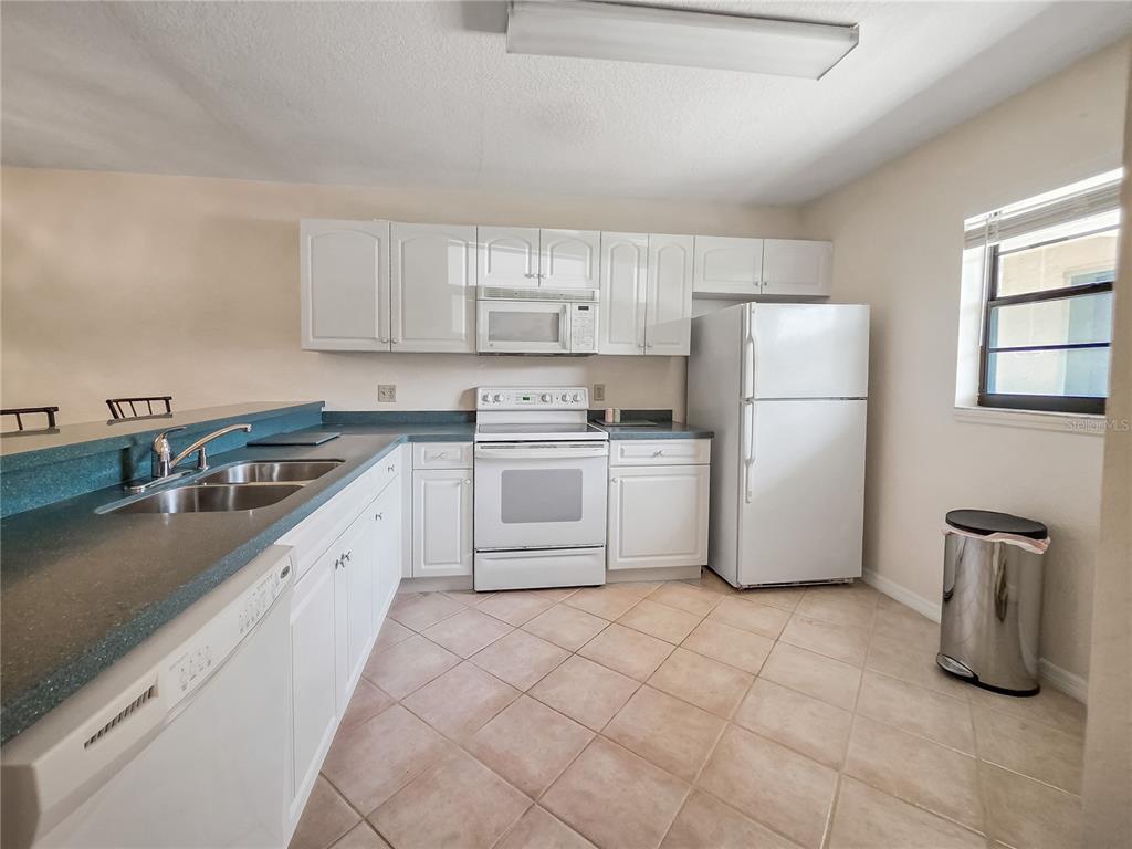 A kitchen features white cabinets, white appliances, a blue countertop, and light-colored tile flooring — 175 KINGS HIGHWAY Bldg 3 UNIT 314, PUNTA GORDA, FL