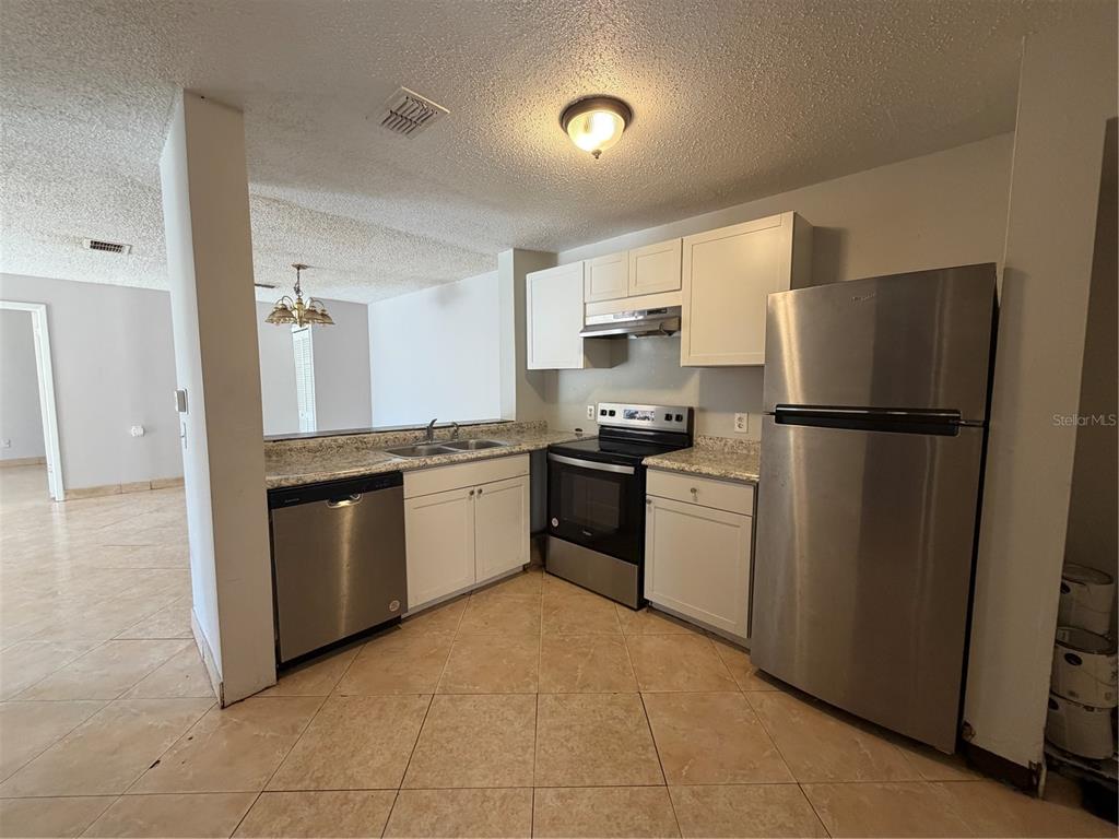 A kitchen with stainless steel appliances, white cabinets, and light-colored tile flooring — 5225 VIA HACIENDA CIRCLE UNIT B115, ORLANDO, FL