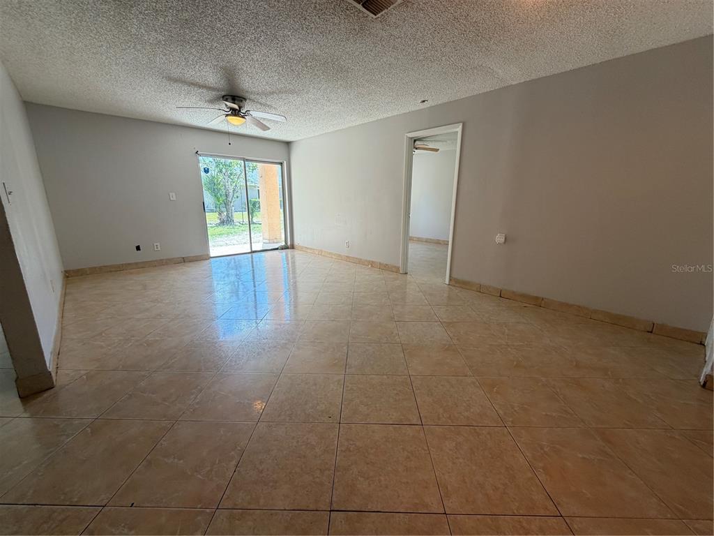 An empty living room features beige tile flooring, a ceiling fan, and a sliding glass door — 5225 VIA HACIENDA CIRCLE UNIT B115, ORLANDO, FL