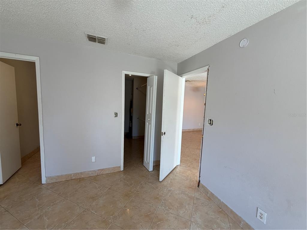An interior view of a room with light gray walls, tile flooring, and three open doorways — 5225 VIA HACIENDA CIRCLE UNIT B115, ORLANDO, FL