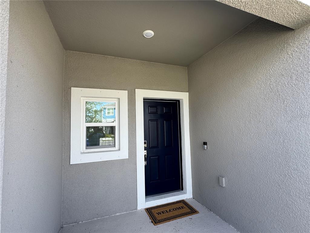 A dark front door and a small window are set into a gray stucco wall — 15148 CUZCORRO COURT, NOKOMIS, FL