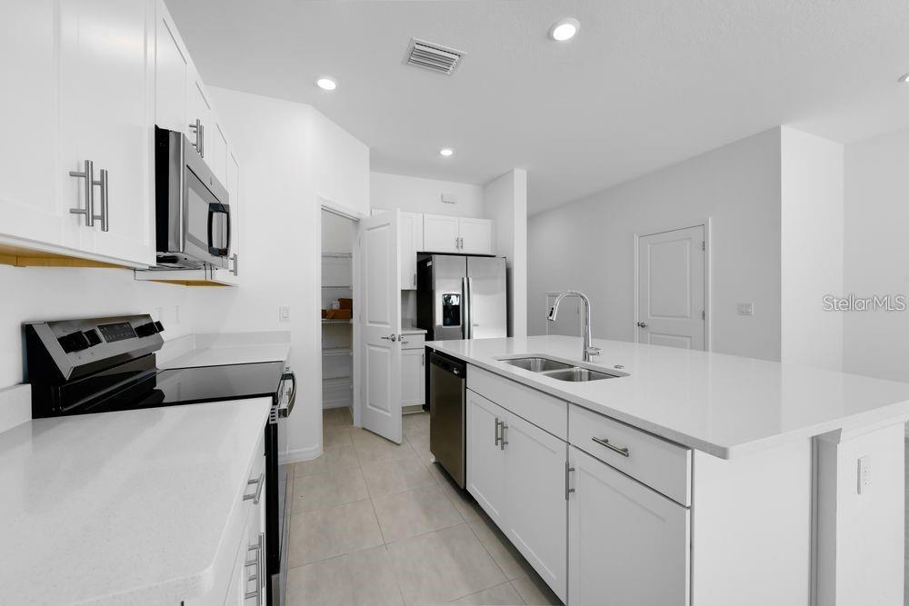 A modern kitchen features white cabinets, stainless steel appliances, and a large central island — 15148 CUZCORRO COURT, NOKOMIS, FL