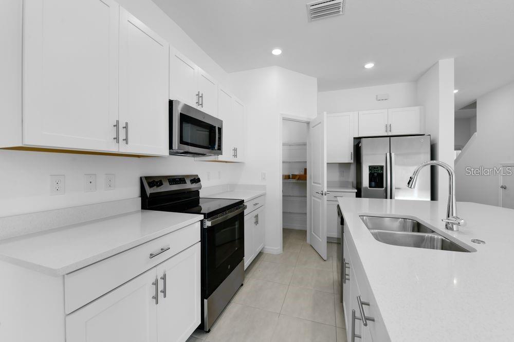 A modern kitchen features white cabinets, stainless steel appliances, a kitchen island, and a pantry — 15148 CUZCORRO COURT, NOKOMIS, FL