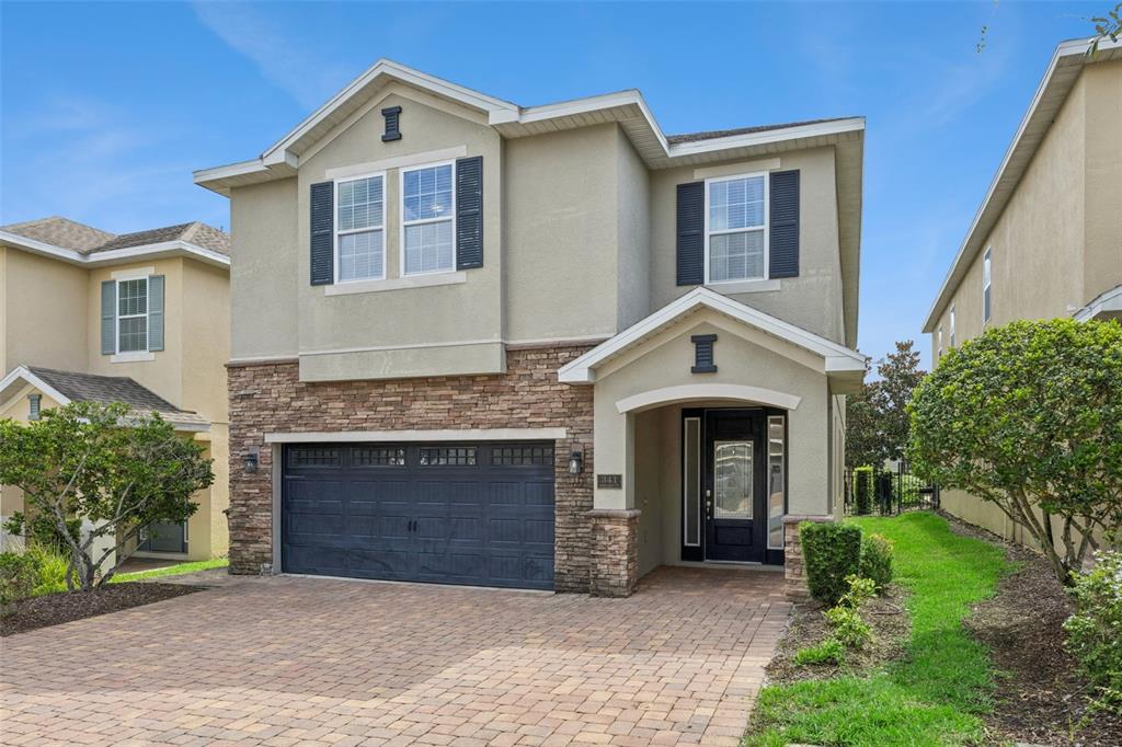 A two-story suburban house with a stone facade, dark garage door, and paver driveway — 341 PENDANT COURT, KISSIMMEE, FL