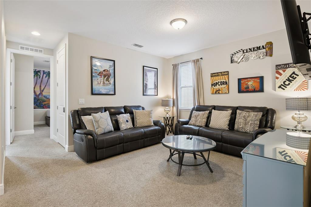 A living room features two dark leather sofas, a glass coffee table, and cinema-themed wall art — 341 PENDANT COURT, KISSIMMEE, FL