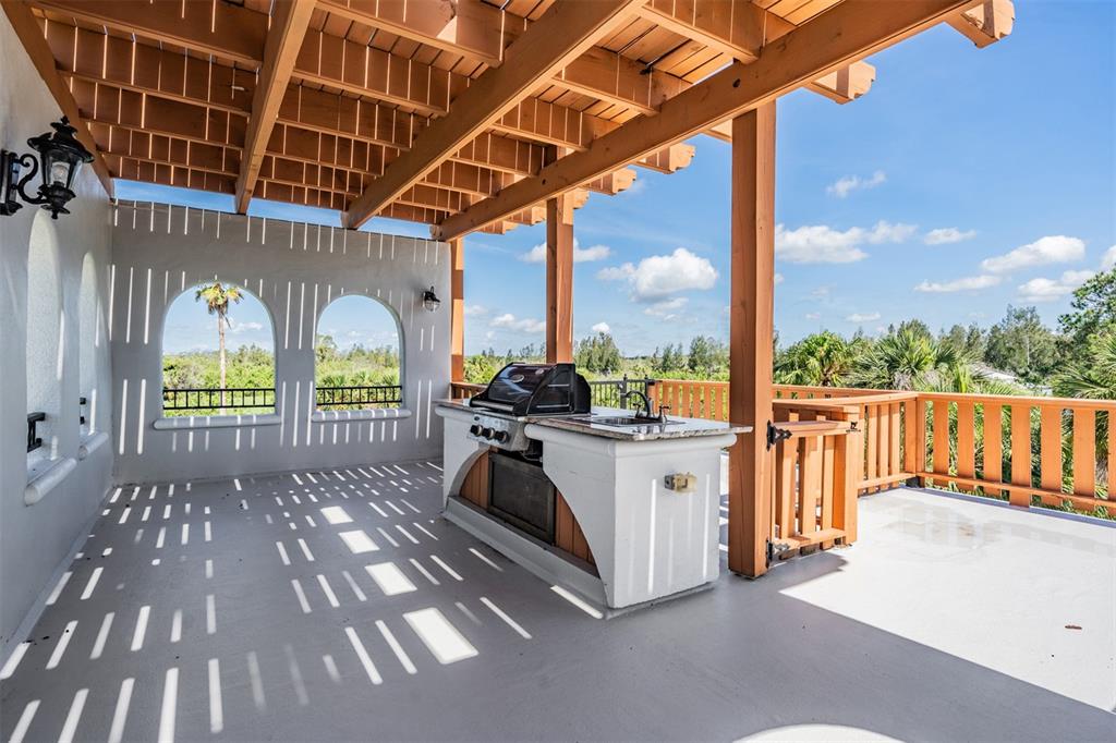 An outdoor covered patio features a built-in grill station, wooden pergola, and scenic landscape views — 4710 TROYDALE ROAD, TAMPA, FL