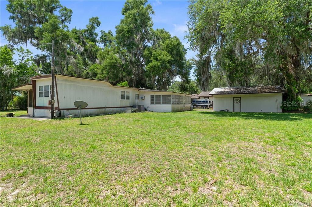 A mobile home and a detached shed sit on a grassy lot with large trees — 8845 E WASHINGTON LANE, FLORAL CITY, FL