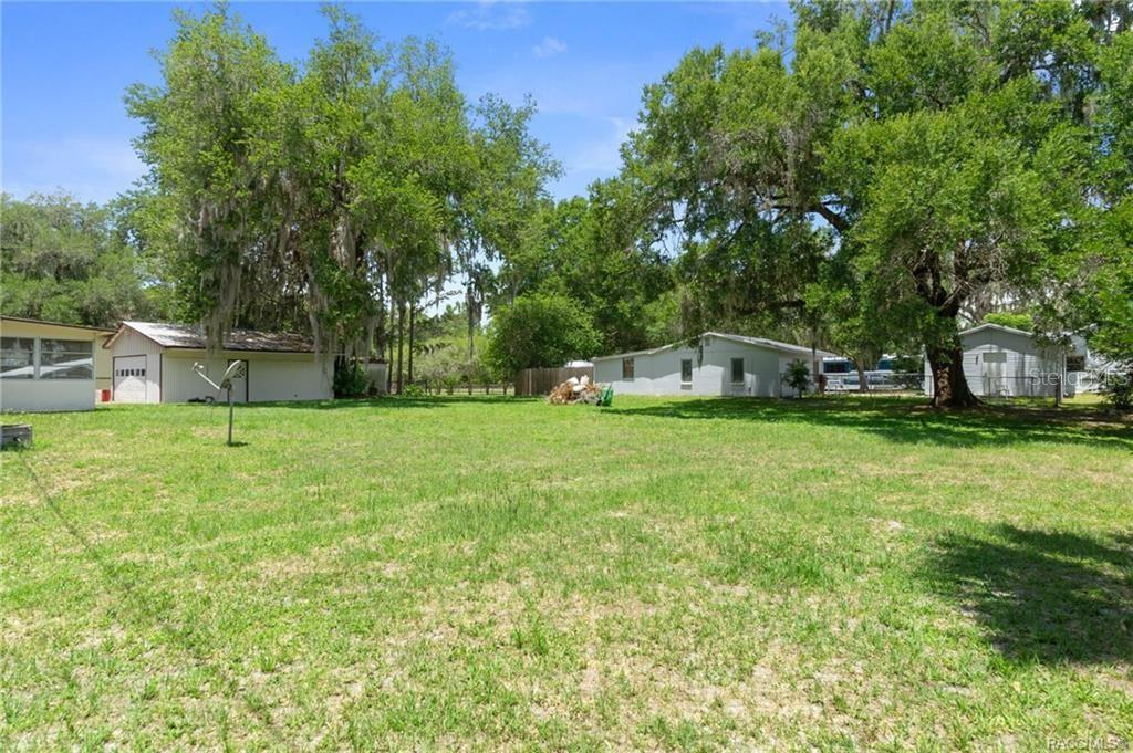 A grassy backyard features several small outbuildings and large trees under a blue sky — 8845 E WASHINGTON LANE, FLORAL CITY, FL