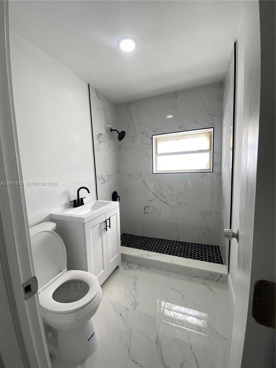 A small bathroom features a white vanity, a toilet, and a walk-in shower with tile — 894 NW 108th St # 1, Miami FL 33168, MIAMI, FL