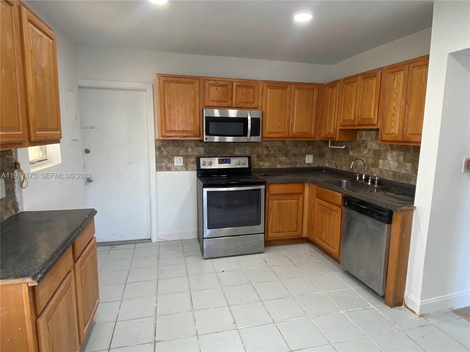 A kitchen features wood cabinets, stainless steel appliances, dark countertops, and light-colored tile flooring — 894 NW 108th St # 1, Miami FL 33168, MIAMI, FL