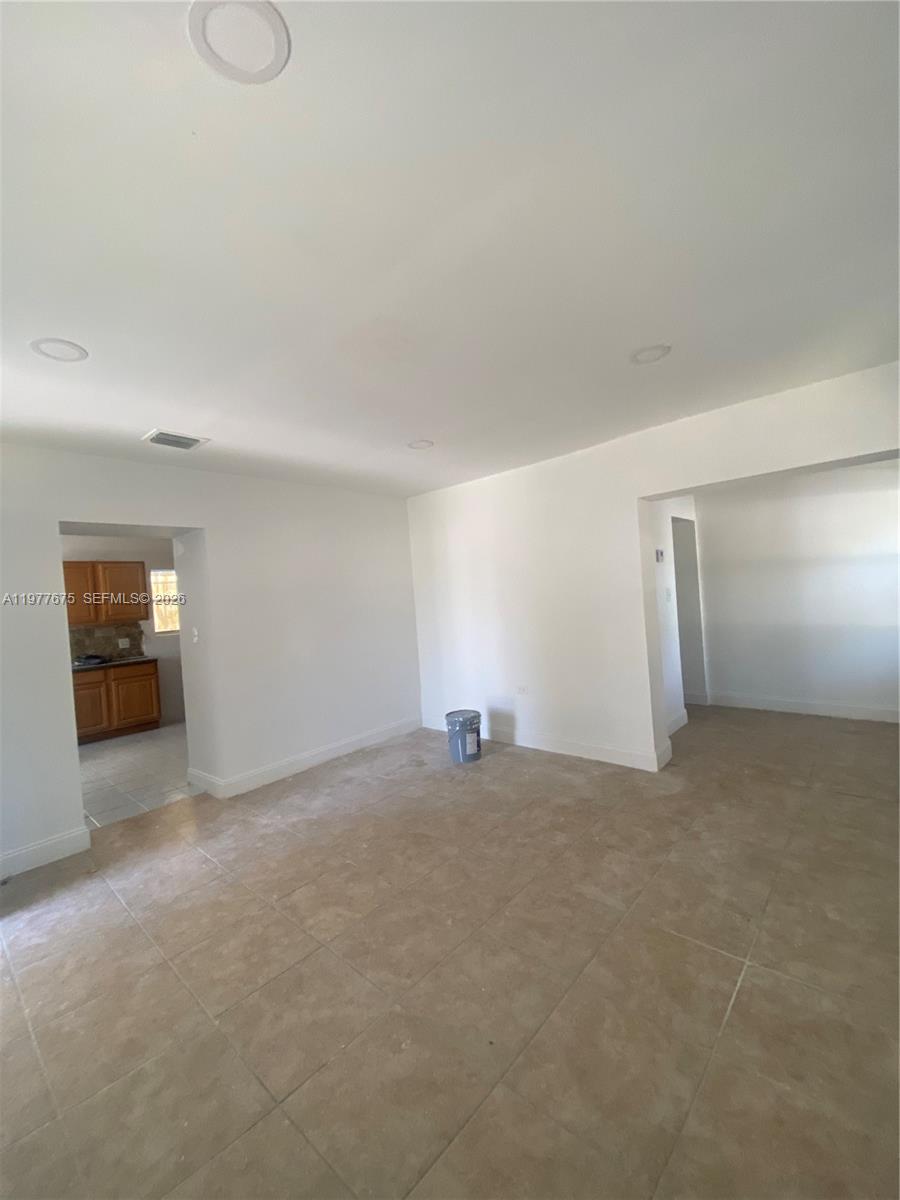 An interior view shows a tiled room with white walls and an adjacent kitchen area — 894 NW 108th St # 1, Miami FL 33168, MIAMI, FL