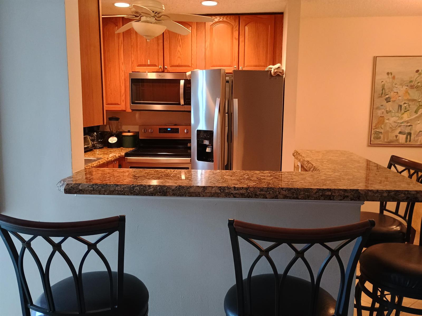 A kitchen features wood cabinets, stainless steel appliances, and a granite-topped breakfast bar with stools — 14716 Canalview Drive # D, Delray Beach FL 33484, DELRAY BEACH, FL