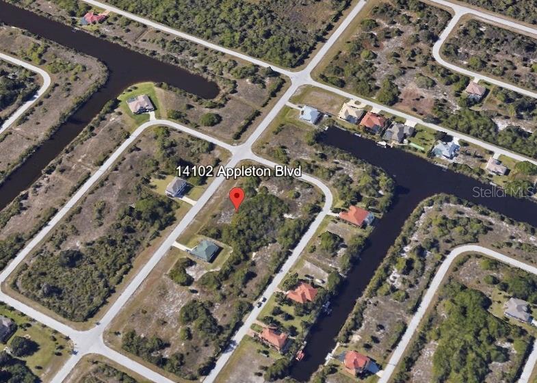 This aerial view shows a vacant residential lot situated between existing houses and a canal — 14102 APPLETON BOULEVARD, PORT CHARLOTTE, FL