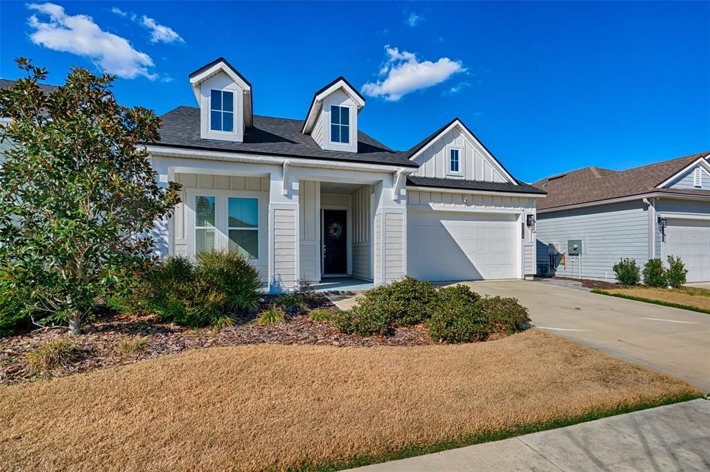 A white house with a two-car garage, two dormer windows, and a landscaped front yard — 12020 SW 30TH AVENUE, GAINESVILLE, FL