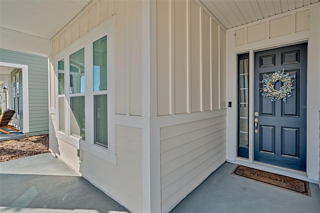 A covered front porch features a dark blue door with a wreath and beige siding — 12020 SW 30TH AVENUE, GAINESVILLE, FL