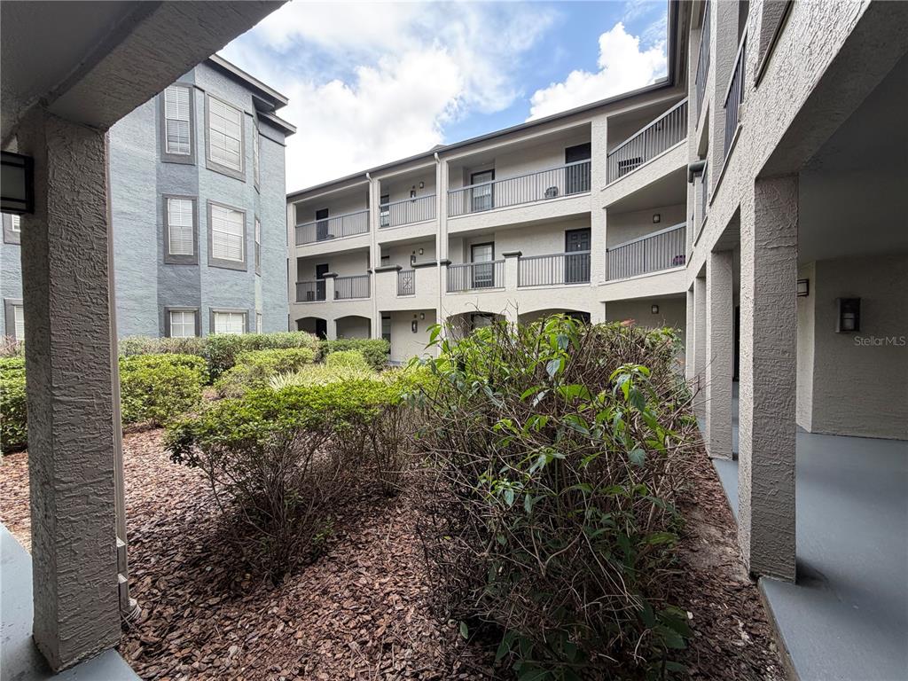 A view of a multi-story apartment building courtyard with landscaping and a covered walkway — 13210 ARBOR ISLE DR UNIT 102, TEMPLE TERRACE, FL
