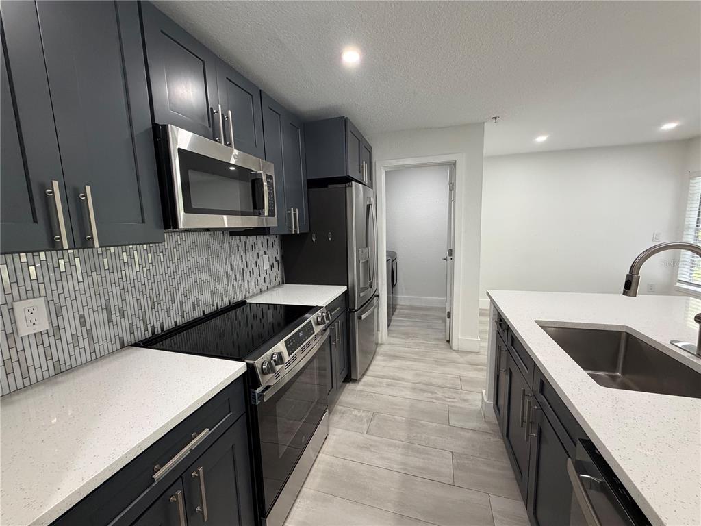 A modern kitchen features dark blue cabinets, stainless steel appliances, and a white quartz countertop — 13210 ARBOR ISLE DR UNIT 102, TEMPLE TERRACE, FL