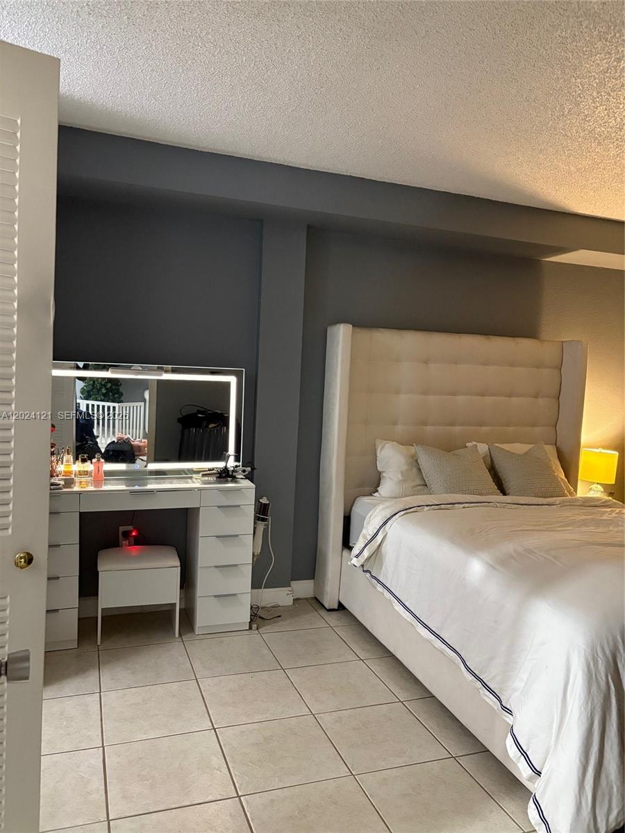 A bedroom features a white vanity with a lighted mirror next to a tufted bed — 10900 SW 104th St # 219, Miami FL 33176, MIAMI, FL