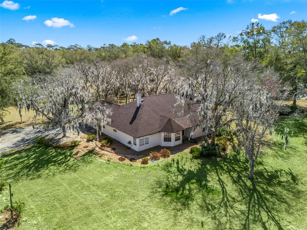 An aerial view of a white house with a dark roof surrounded by mossy trees — 7368 NW 14TH STREET, OCALA, FL