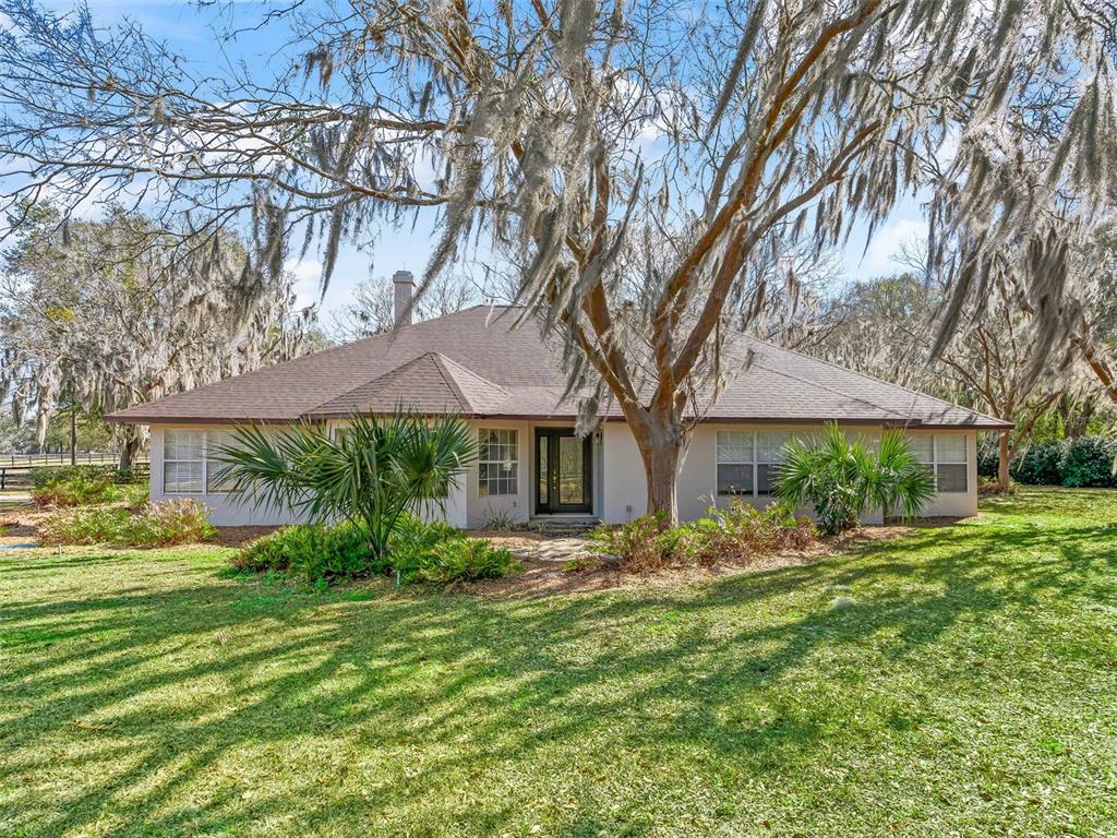 A single-story house with a brown roof sits on a grassy lawn with trees — 7368 NW 14TH STREET, OCALA, FL