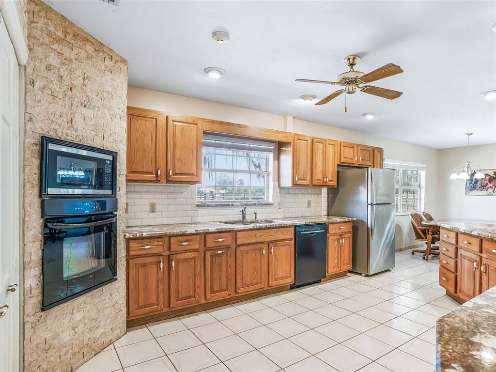 A kitchen features oak cabinets, stainless steel appliances, a stone wall, and white tile flooring — 7368 NW 14TH STREET, OCALA, FL