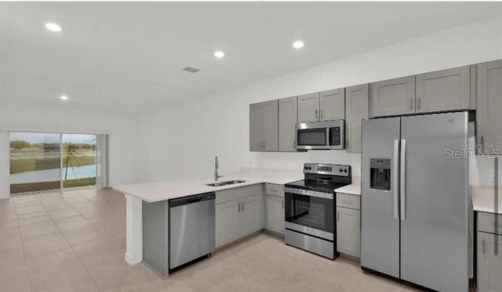A modern kitchen features gray cabinets, stainless steel appliances, and an island with a sink — 2081 VIEWFINDER ST, KISSIMMEE, FL