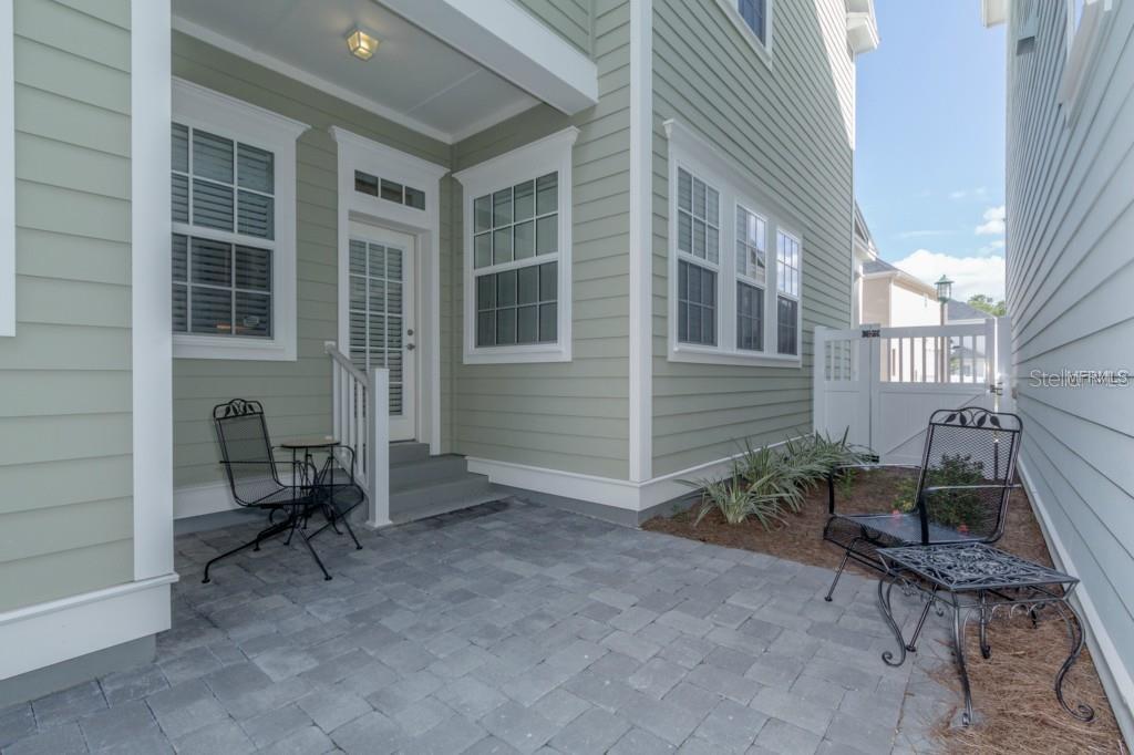 A paved patio area sits beside a light green house with a white door and fence — 1596 CASTILE STREET, CELEBRATION, FL