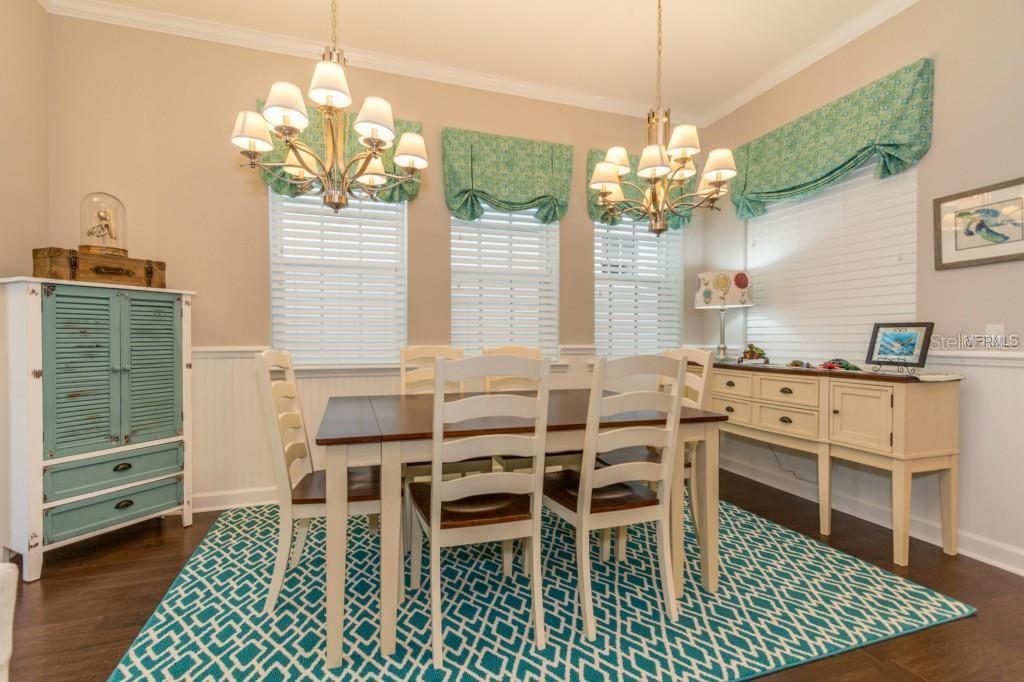 A dining room features a wooden table, white chairs, two chandeliers, and a patterned rug — 1596 CASTILE STREET, CELEBRATION, FL