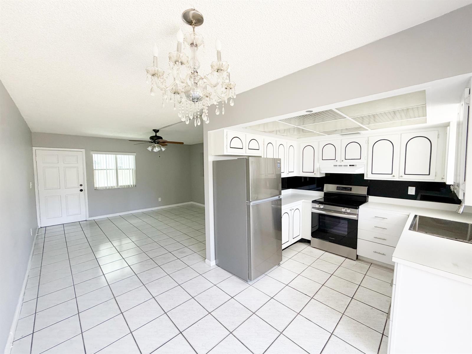 A kitchen with white cabinets and stainless steel appliances opens into a tiled living area — 320 SW 1st Street # 2, Pompano Beach FL 33060, POMPANO BEACH, FL