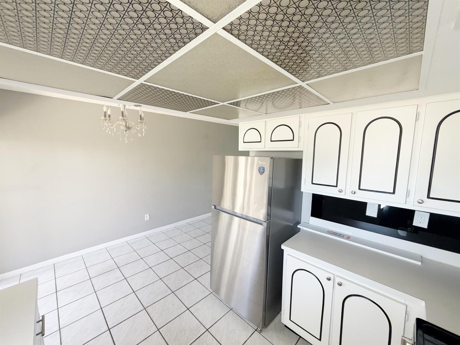 A kitchen features white cabinets with black trim, a stainless steel refrigerator, and patterned ceiling tiles — 320 SW 1st Street # 2, Pompano Beach FL 33060, POMPANO BEACH, FL