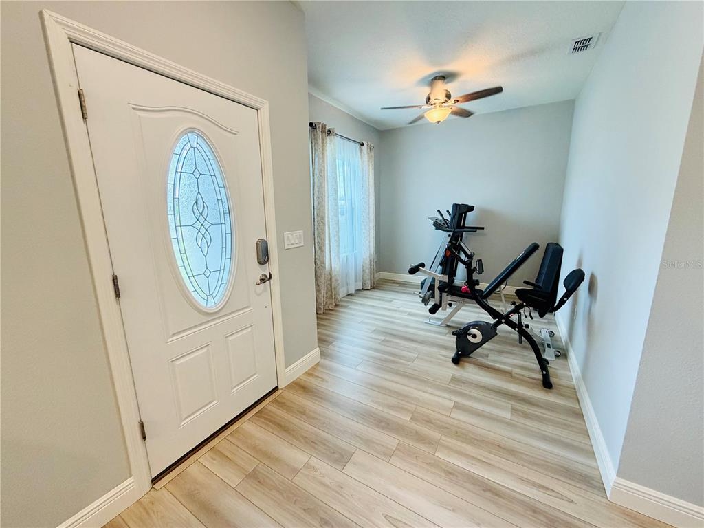 An entryway with light wood-look flooring, a white front door, and a home gym setup — 5149 SW 107TH LOOP, OCALA, FL