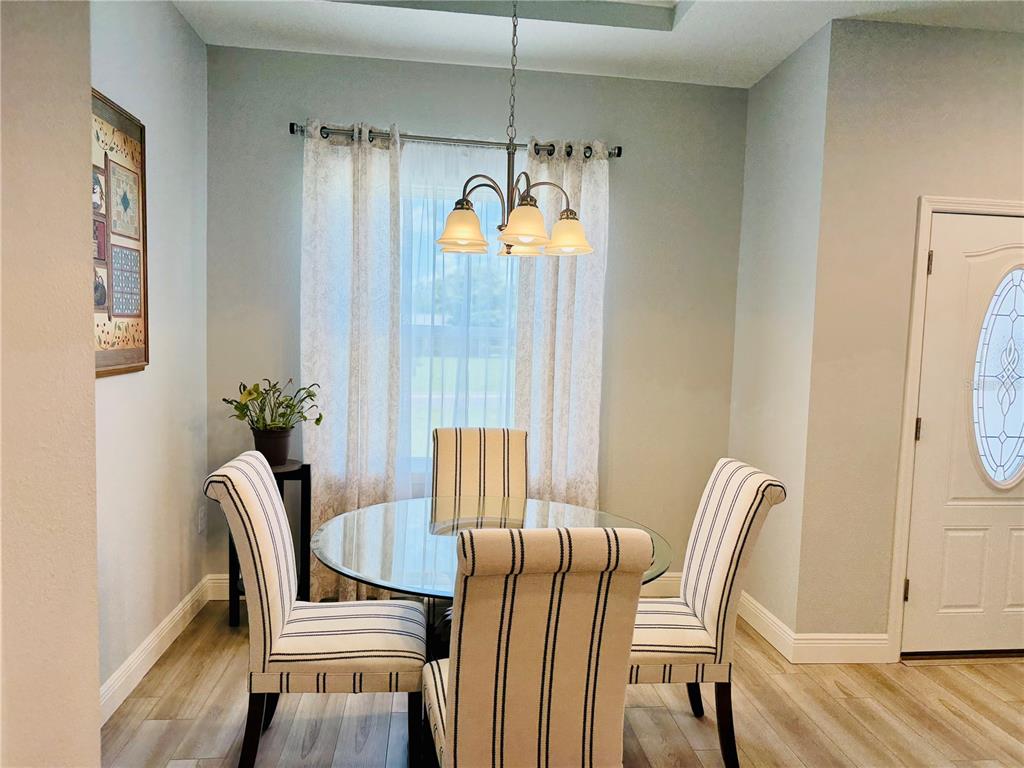 A dining area features a glass-topped table, striped chairs, a chandelier, and light wood flooring — 5149 SW 107TH LOOP, OCALA, FL