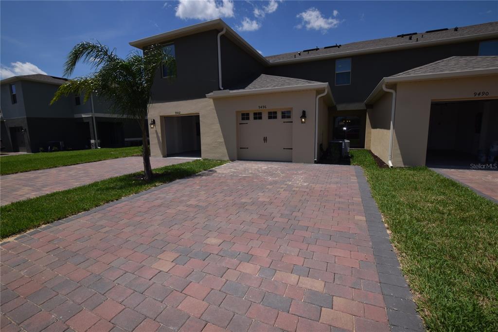 A paved driveway leads to the garages of a multi-unit residential building under a blue sky — 9496 BAUER ALLEY, WINTER GARDEN, FL