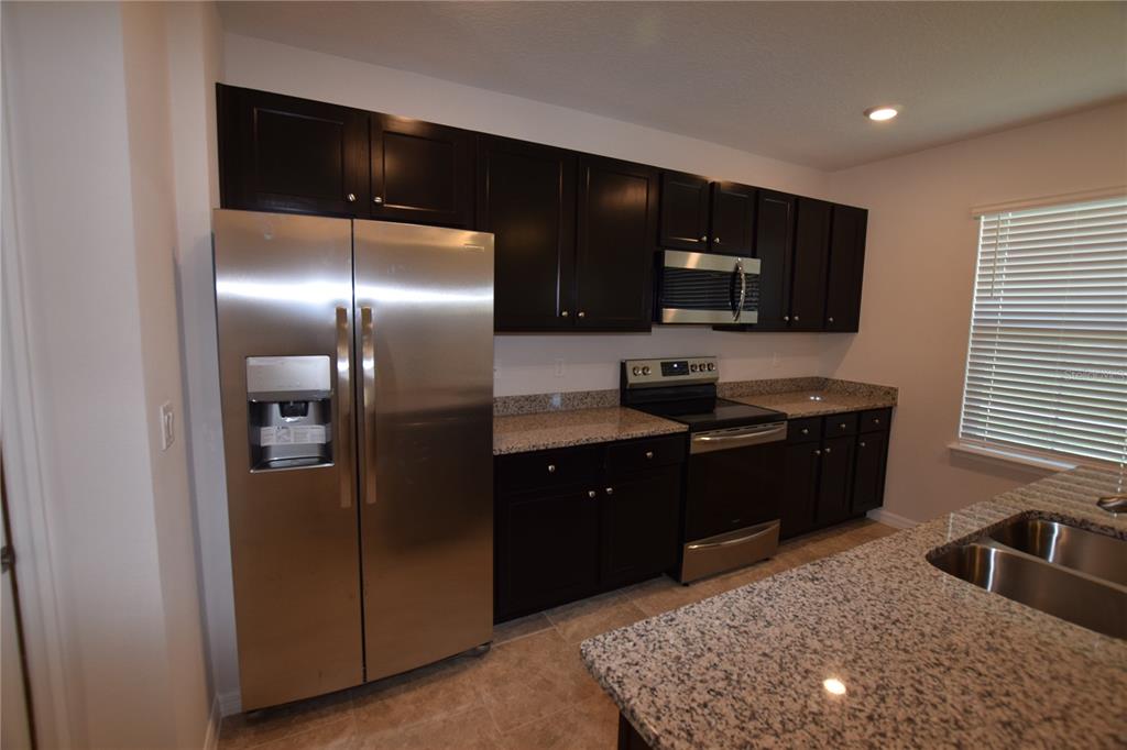 A kitchen features dark wood cabinets, granite countertops, and stainless steel appliances — 9496 BAUER ALLEY, WINTER GARDEN, FL
